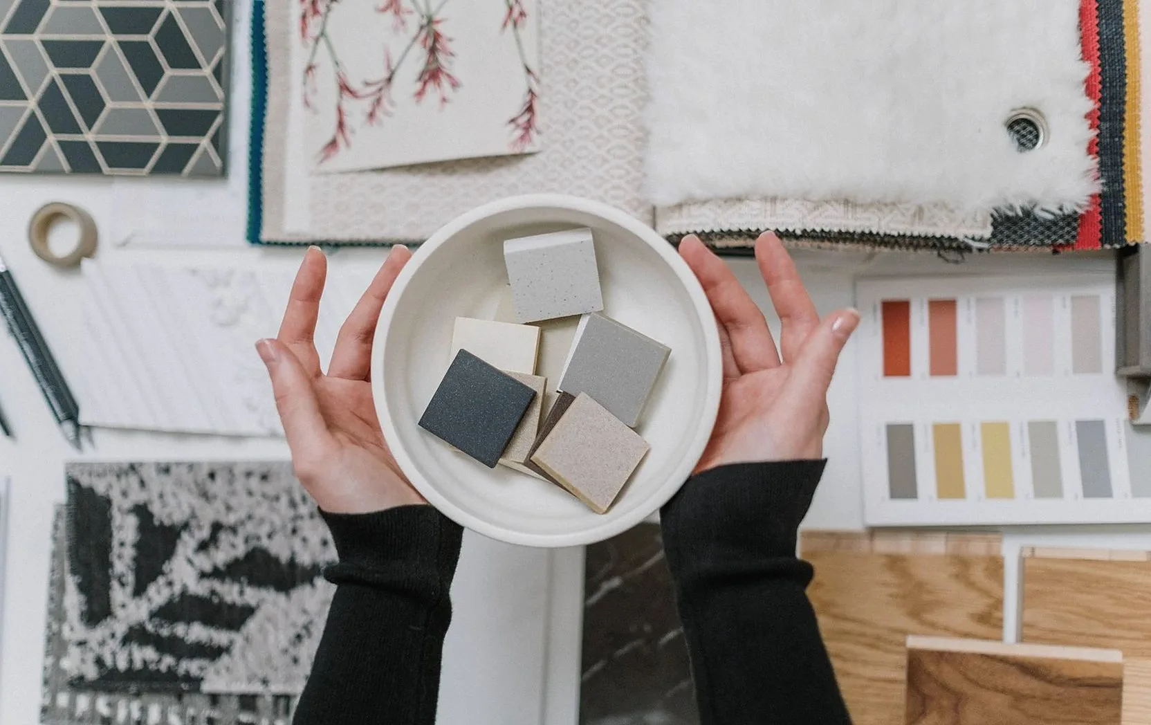 Hands holding a bowl of tile samples over fabric and colour cards