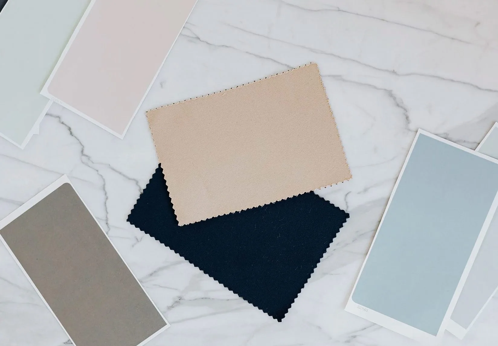Fabric and paper swatches in beige, navy, grey and pale blue on marble