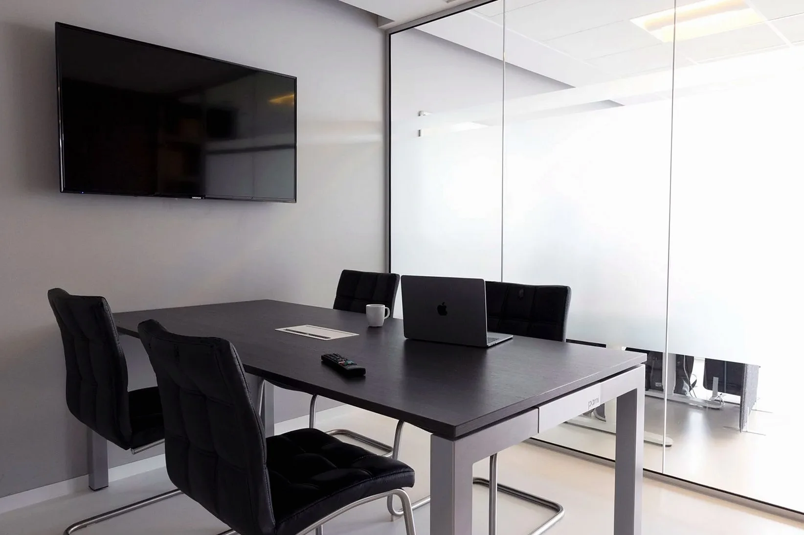 Meeting room with a dark table, black chairs and a wall-mounted screen