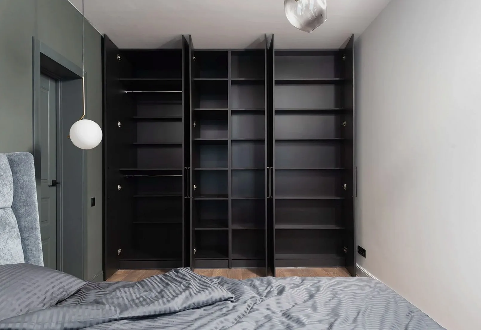 Dark built-in wardrobe beside a bed with grey bedding